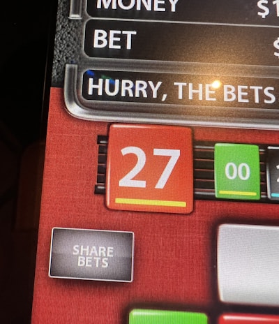 A digital display screen showing a casino betting interface, with text prompting to hurry bets and a highlighted number 27 in red. There are options for betting amounts and a 'share bets' button.