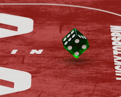 Two green dice with rounded edges are positioned on a red surface that seems to be part of a game board. The surface has white text and numbers on it, including the word 'LUCKYTOPSPIN' in capital letters.